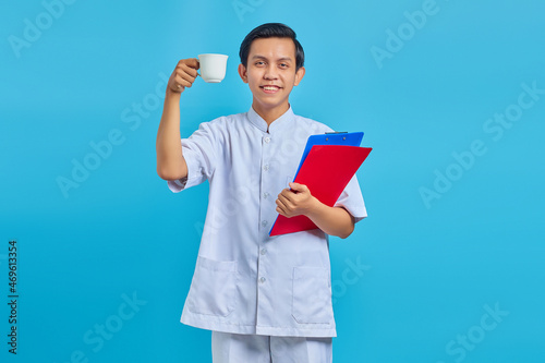 Smiling young male nurse holding folder and cup over blue background