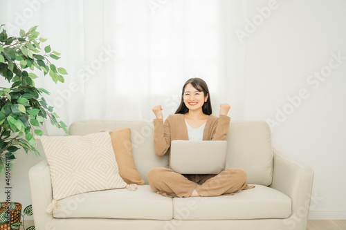 家でノートパソコンを使う女性（ソファ・ガッツポーズ） 