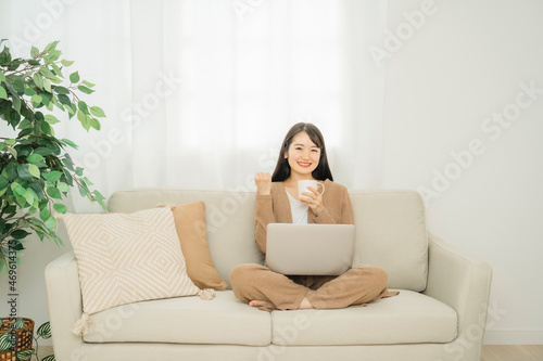 家でノートパソコンを使う女性（ソファ・ガッツポーズ）  © buritora