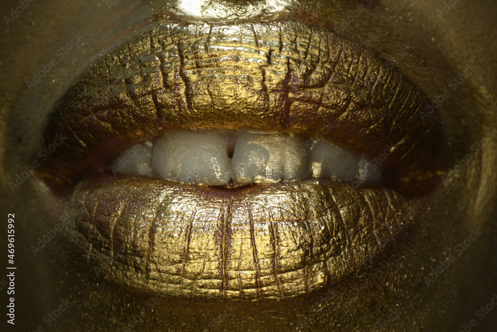Obraz premium Golden lips macro close up. Gold lips. Gold paint from the mouth. Golden lips on woman mouth with make-up. Sensual and creative design for golden metallic.