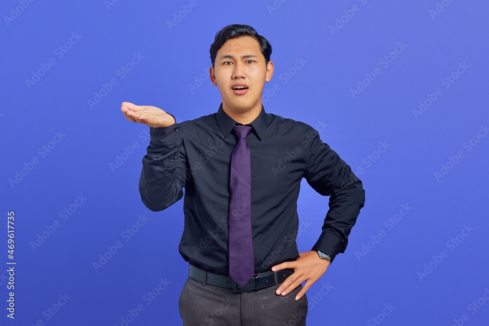 Portrait of shocked young handsome businessman showing copy space on palm on purple background Portrait of shocked young handsome businessman showing copy space on palm on purple background