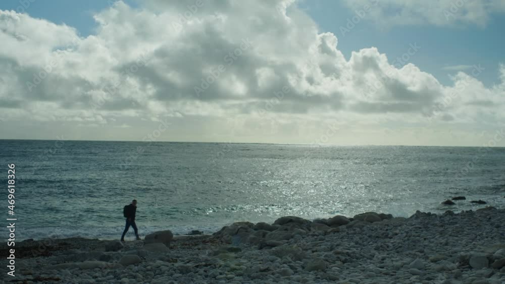 4K Slow motion panoramic landscape shot of a man walking on the rocky beach of Church Ope, on the island of Portland, in Dorset, England, on a sunny day. 4K Slow motion panoramic landscape shot of a man walking on the rocky beach of Church Ope, on the island of Portland, in Dorset, England, on a sunny day.