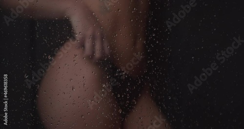 4K close up of an athletic female model in underwear with flat belly taking a shower behind the shower screen while the shower drops fall on her body. Concept of sexy women wet in the shower. photo