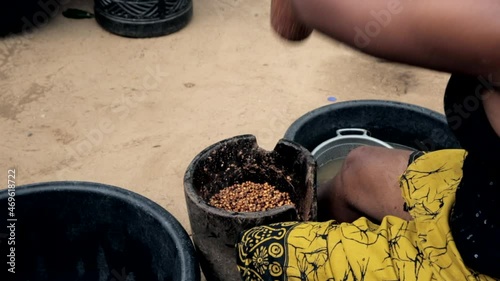 Woman in rural Nigeria, West Africa pounding tiger nut into flour in a motor and pestle - over shoulder view photo