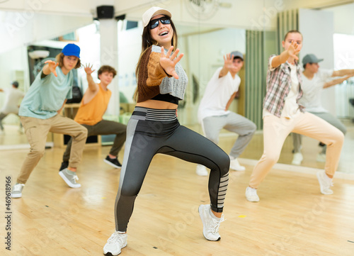 Portrait of cheerful hispanic teenage girl practicing hip-hop movements during group dance lesson in studio.
