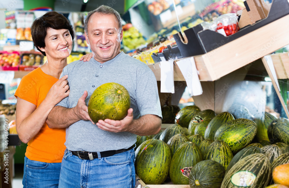 Fototapeta premium Adult happy male and female are choosing green melons in the store.