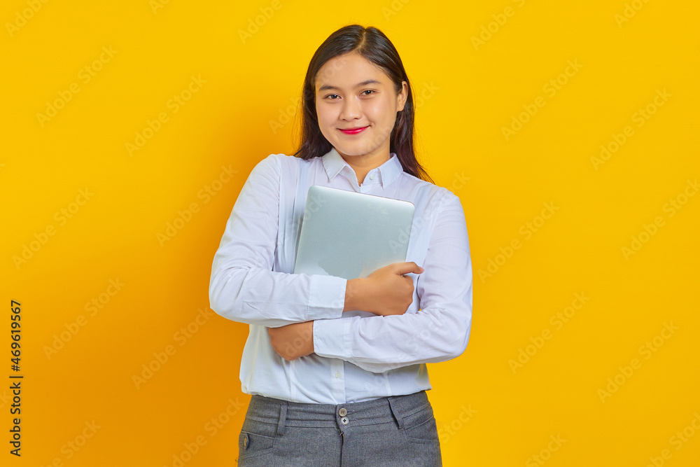 Photo of cheerful young business woman with confident face and holding laptop over yellow background Photo of cheerful young business woman with confident face and holding laptop over yellow background