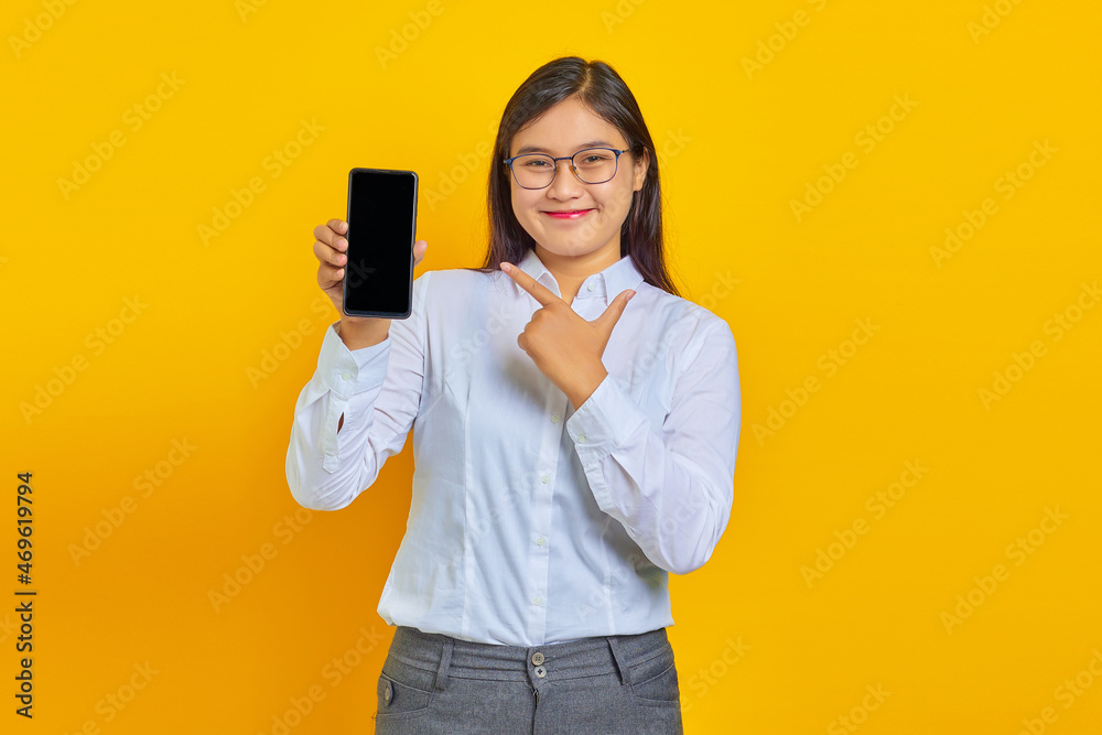 Photo of cheerful business woman showing blank smartphone screen and pointing at it while looking at camera Photo of cheerful business woman showing blank smartphone screen and pointing at it while looking at camera