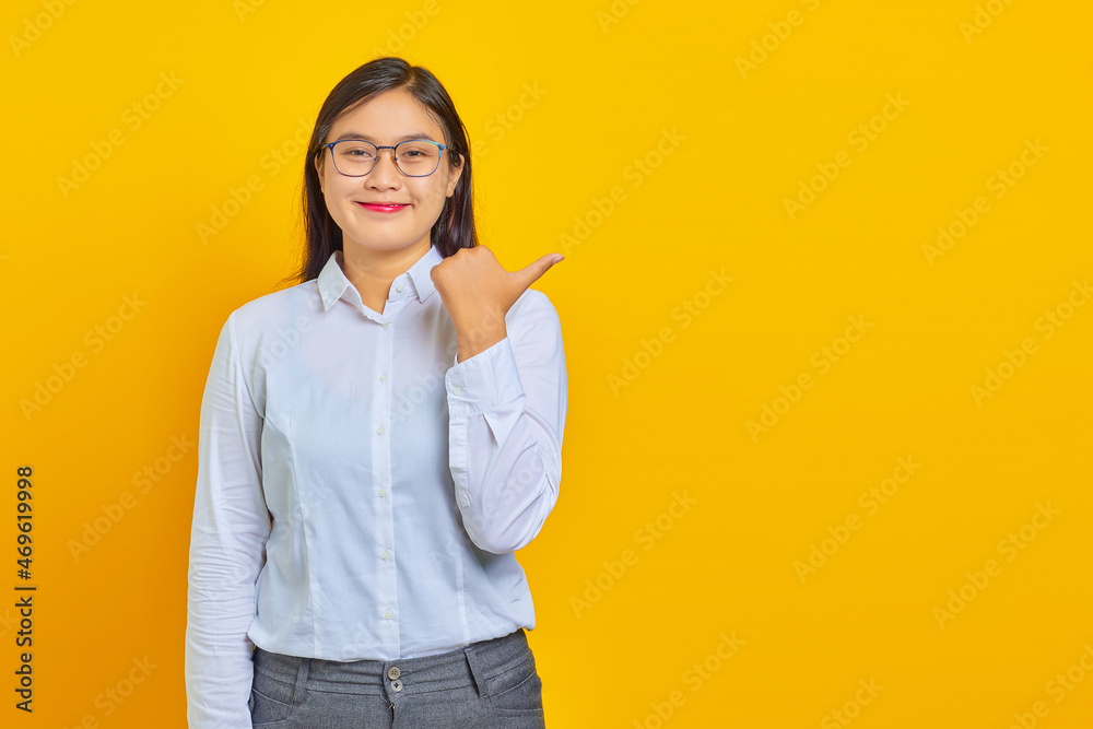 Beautiful young business woman smiling with confident face pointing to empty space with finger on yellow background Beautiful young business woman smiling with confident face pointing to empty space with finger on yellow background