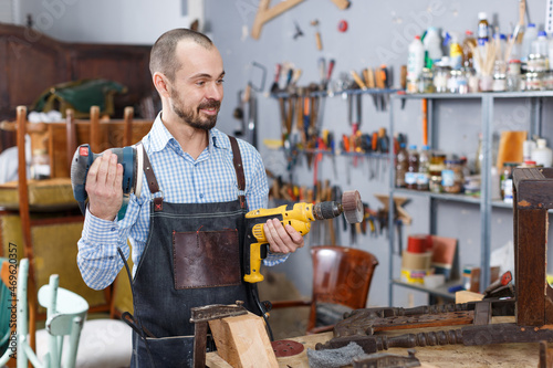 Portrait of young cheerful furniture restorer holding tools in hand in woodwork studio photo