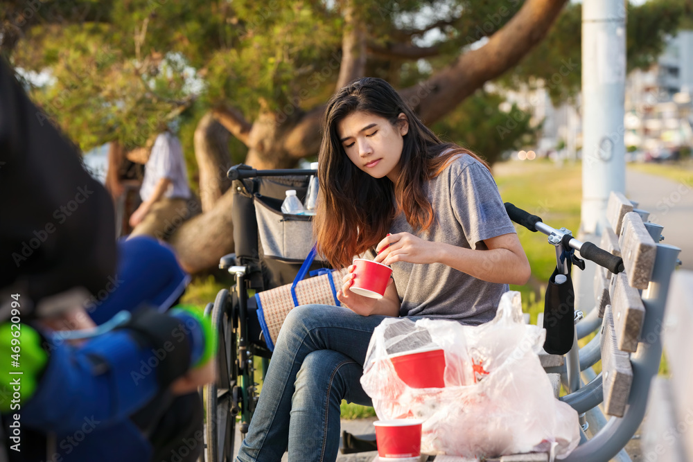 Obraz premium Biracial teen girl on park bench outdoors eating takeout food