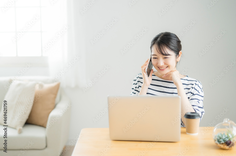 家でテレワークする女性(スマホで電話)
家でテレワークする女性(スマホで電話)