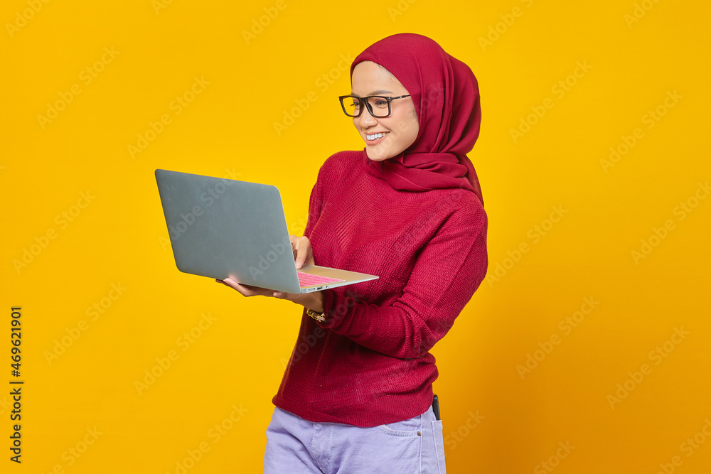 Portrait of smiling asian woman holding laptop over yellow background