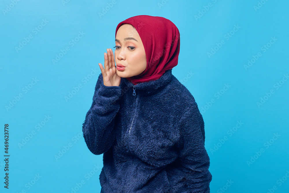 Portrait of beautiful Asian woman keeps hand near mouth and whisper secret on blue background Portrait of beautiful Asian woman keeps hand near mouth and whisper secret on blue background