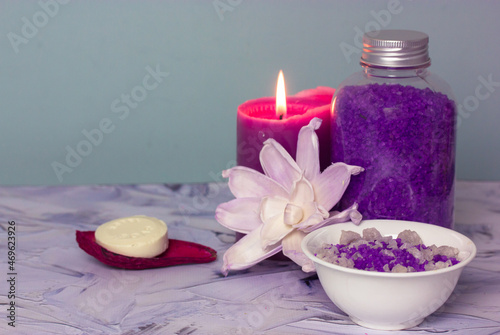 Composition with a jar of purple lavender sea salt  soap bar  burning lilac candle and beautiful flower. Spa procedure  body  facial care. Cosmetic products. Bathing treatments in a beauty salon.