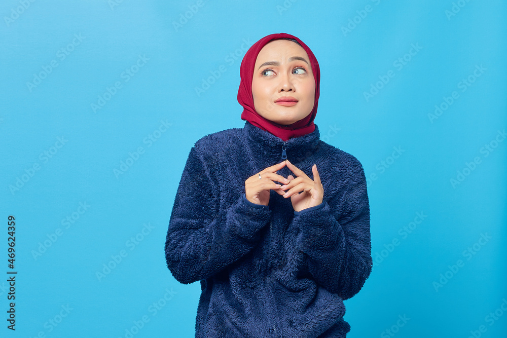Smiling young Asian woman rubbing hand while looking at copy space on blue background Smiling young Asian woman rubbing hand while looking at copy space on blue background
