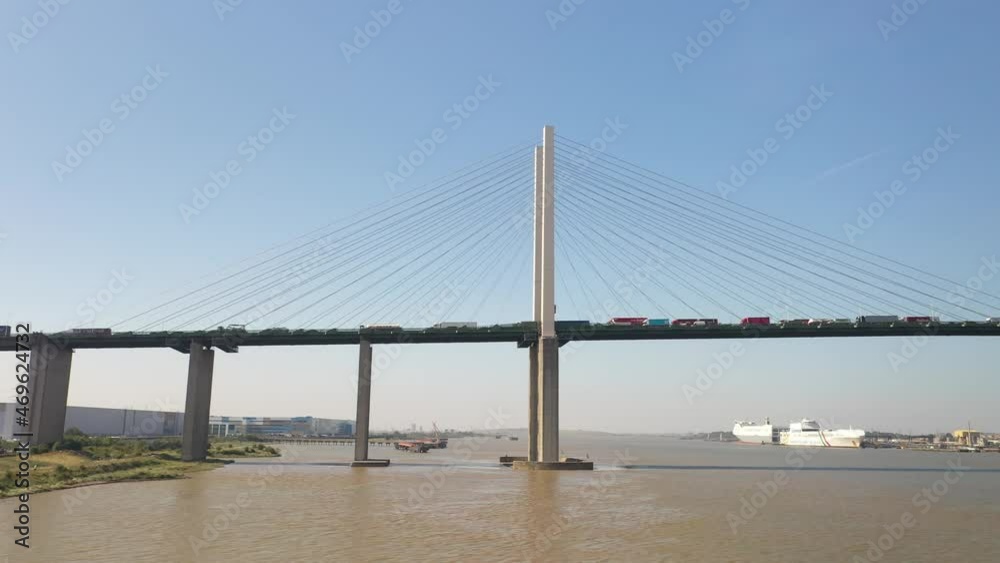 Sliding low angle view of busy cable-stayed road bridge over river. Big cargo ships in background Sliding low angle view of busy cable-stayed road bridge over river. Big cargo ships in background