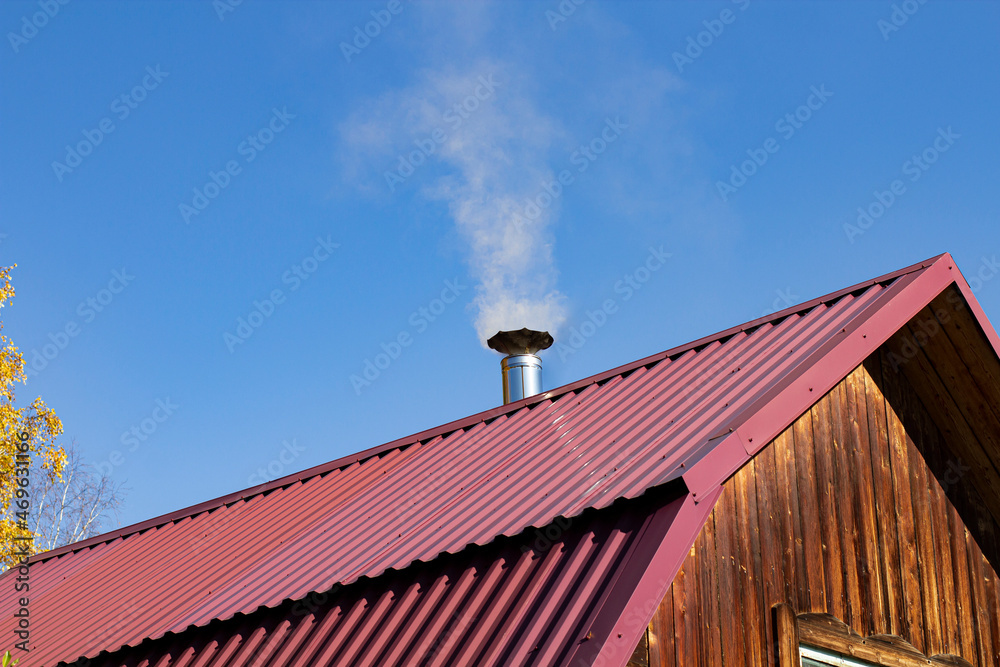 Steel roof of a private house with chimney and smoke against the backdrop of a beautiful blue sky. Steel roof of a private house with chimney and smoke against the backdrop of a beautiful blue sky.