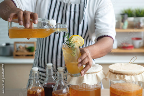 Konstfotografi Man in apron pouring kombucha from bottle to made Kombucha cocktail, lemon and r