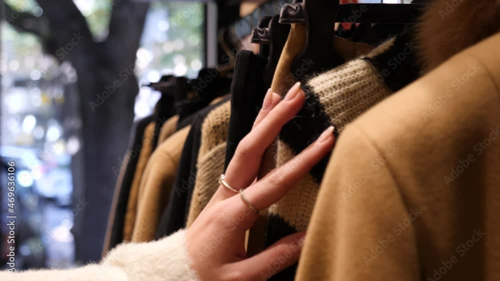 Mano che accarezza vestiti in un negozio di abbigliamento. 
Abiti appesi sulle stampelle in un centro commerciale.