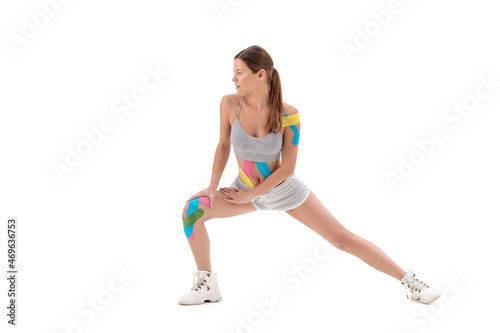 kinesiology tape rehabilitation and health of athletes. girl doing exercises isolated on white isolated background. On the shoulder, belly and knee sticky colored ribbon.