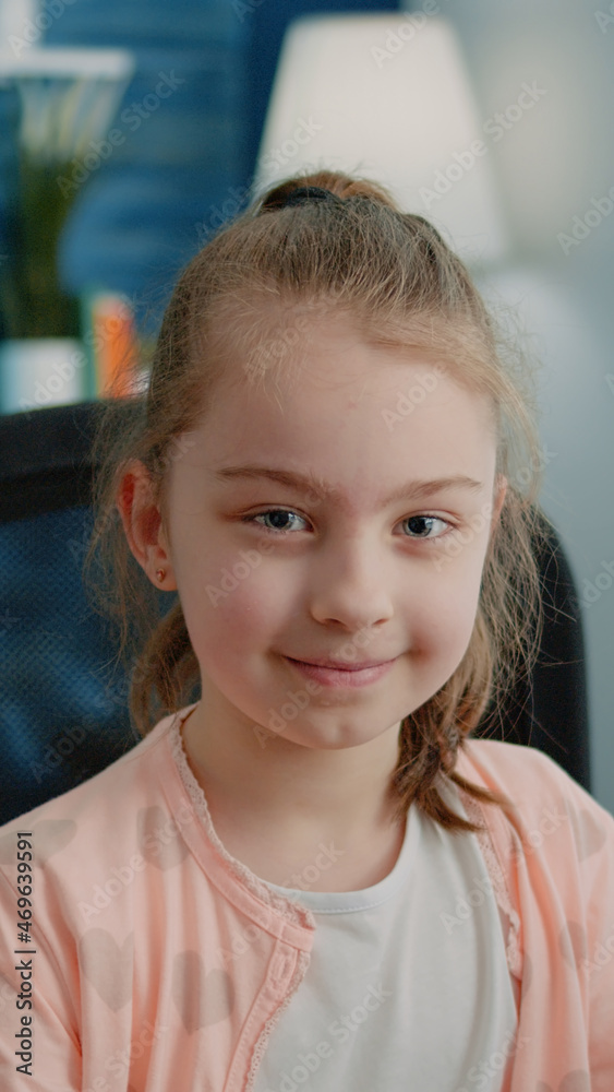 Portrait of little child smiling and looking at camera while sitting at desk. Close up of cheerful girl prepared for remote school work on computer at home. Pupil with education Portrait of little child smiling and looking at camera while sitting at desk. Close up of cheerful girl prepared for remote school work on computer at home. Pupil with education