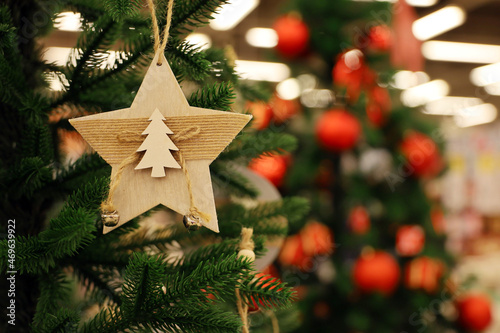 Christmas tree with wooden toy in star shape on a branch. New Year decorations on blurred lights background