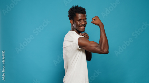 Athletic person flexing biceps muscles on camera in studio. Trained man showing musculature on arms while standing over isolated background. Athlete with muscular body from fitness