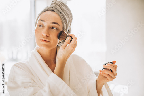Photos Young woman applying blush and looking into the mirror