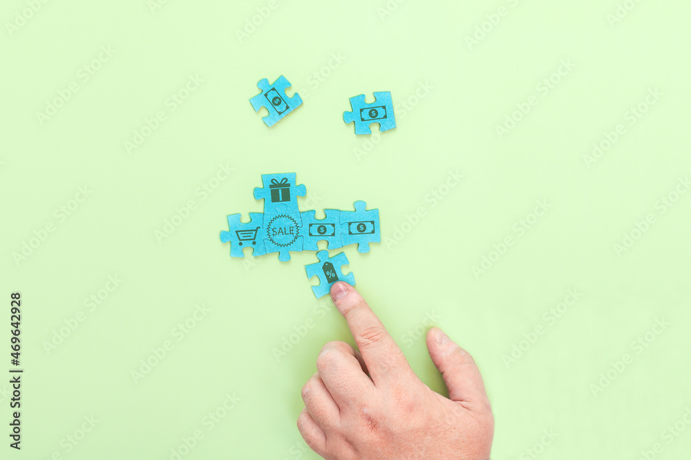 Businessman connecting pieces of a puzzle with the image of dollars and inscription SALE Businessman connecting pieces of a puzzle with the image of dollars and inscription SALE