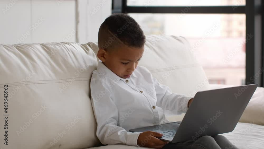 Little Black Boy Using Laptop While Sitting On Couch At Home Little Black Boy Using Laptop While Sitting On Couch At Home