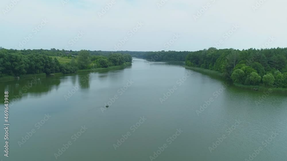 Aerial view beautiful nature forest and lake in which fisherman is fishing sitting on an inflatable boat in the middle of the lake. Drone wide shot adult man in the middle of a pond Aerial view beautiful nature forest and lake in which fisherman is fishing sitting on an inflatable boat in the middle of the lake. Drone wide shot adult man in the middle of a pond