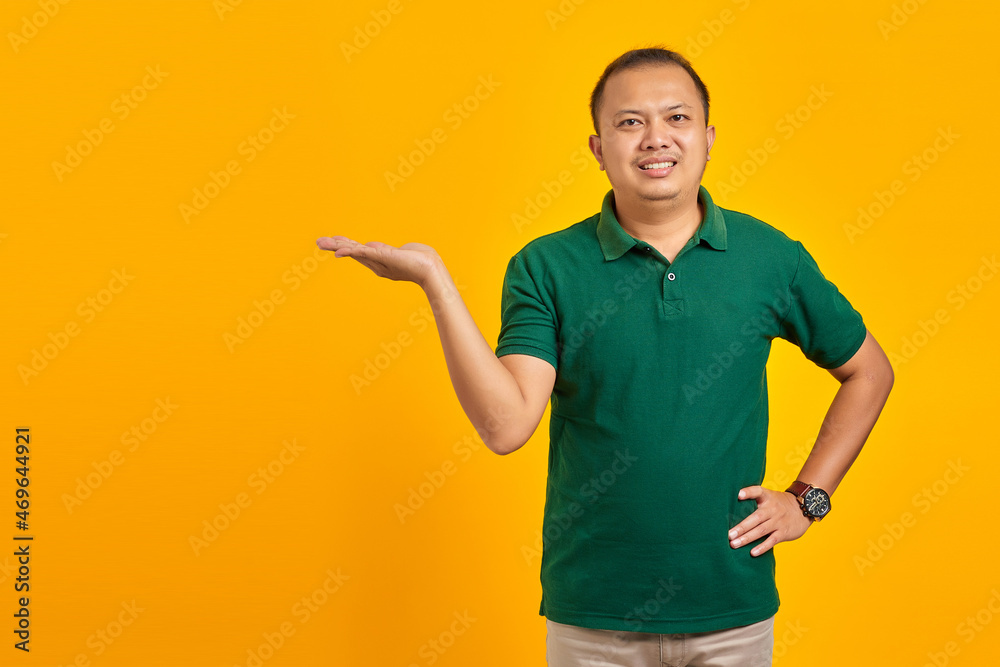Smiling young handsome man showing copy space on palm on yellow background Smiling young handsome man showing copy space on palm on yellow background