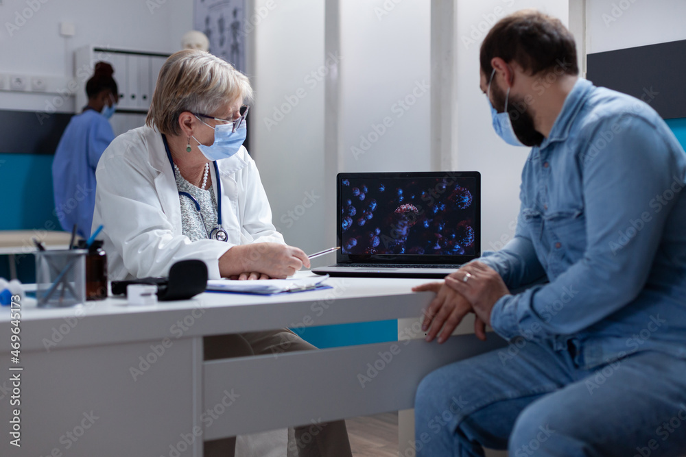 Patient and specialist with face mask looking at virus illustration on laptop, explaining coronavirus bacteria and symptoms. General practitioner showing covid 19 animation for healthcare. Patient and specialist with face mask looking at virus illustration on laptop, explaining coronavirus bacteria and symptoms. General practitioner showing covid 19 animation for healthcare.