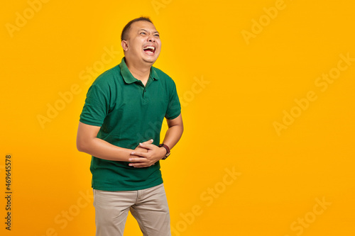 Attractive asian young man laughing out loud at funny on yellow background