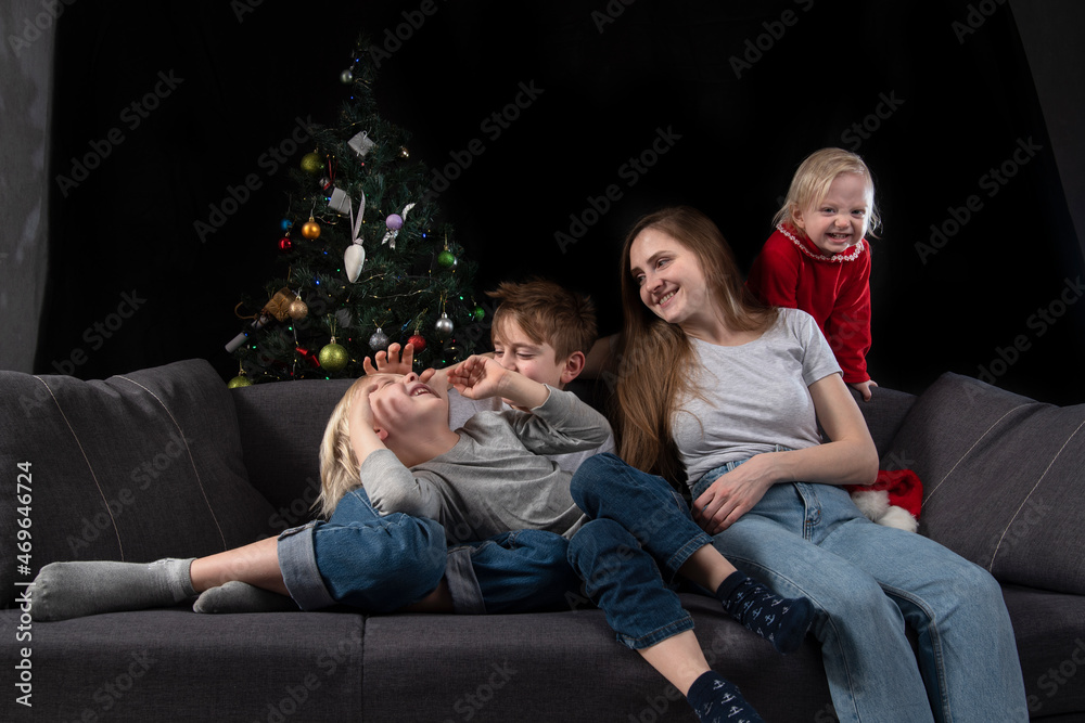 Naklejka premium Cozy family evening - mom and three happy smiling children against the background of the Christmas tree