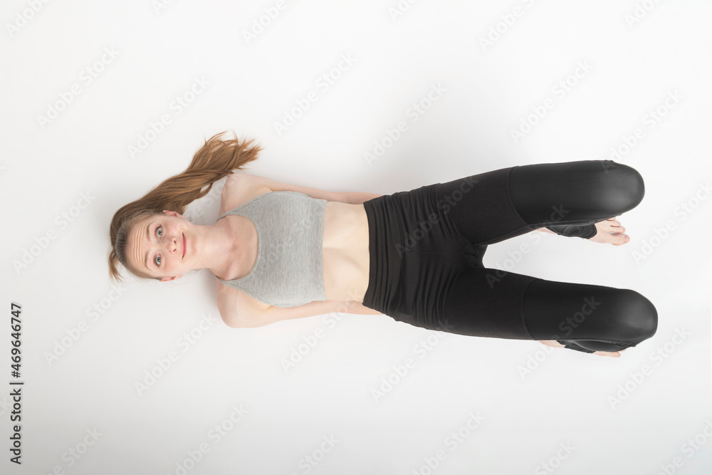 Cheerful young girl with funny face is engaged in yoga, gymnastics, stretching on white background. Top view. Cheerful young girl with funny face is engaged in yoga, gymnastics, stretching on white background. Top view.