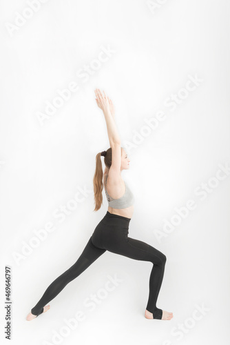 Virabhadrasana I. Warrior I Pose. Attractive woman doing yoga on white background. Girl in sportswear is engaged in fitness. Vertical frame