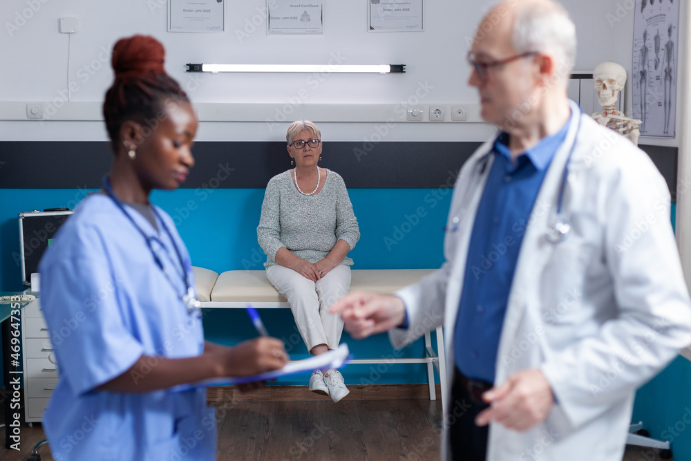 Old person sitting on bed in medical office, waiting to receive assistance and support from doctor and nurse. Senior woman with disease having consultation appointment with physician Old person sitting on bed in medical office, waiting to receive assistance and support from doctor and nurse. Senior woman with disease having consultation appointment with physician