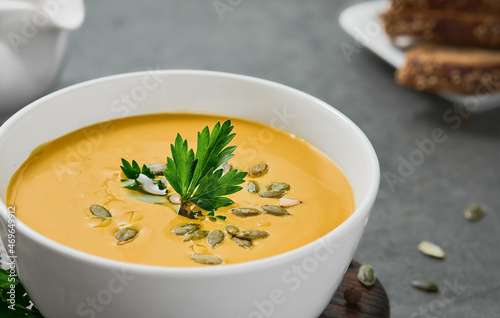 Pumpkin and carrot soup with olive oil, pumpkin seeds and parsley on gray background, close-up, selective sharpening on parsley