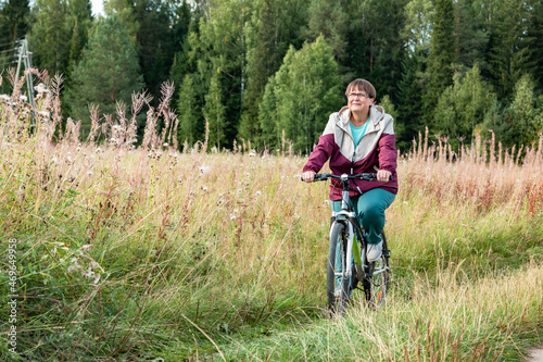 Cheerful grandmother rides a bicycle in nature.
