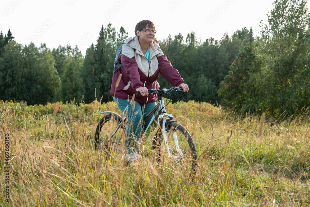 Obraz premium Cheerful grandmother rides a bicycle in nature.