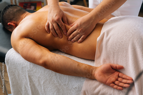 Close-up top view of professional male masseur with strong hands massaging side of back to muscular sports man lying on stomach, at massage table in luxury salon. Concept of healthy lifestyle and rest photo