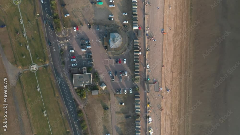 Beach, straight walkway, parked cars and busy road. Top down panning footage of coast