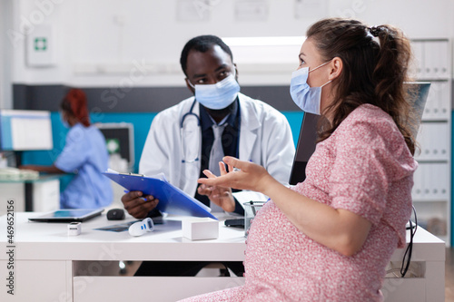 Woman expecting child and having discussion with physician about pregnancy and healthcare. General practitioner giving medical advice to pregnant patient during coronavirus pandemic