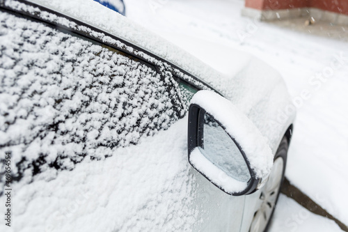 A snow-covered car stands on the street in winter. Snow on car windows