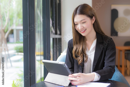 Young Asian professional  working female in a black suit is working on an tablet on the table smiling happily in the office and working at home.