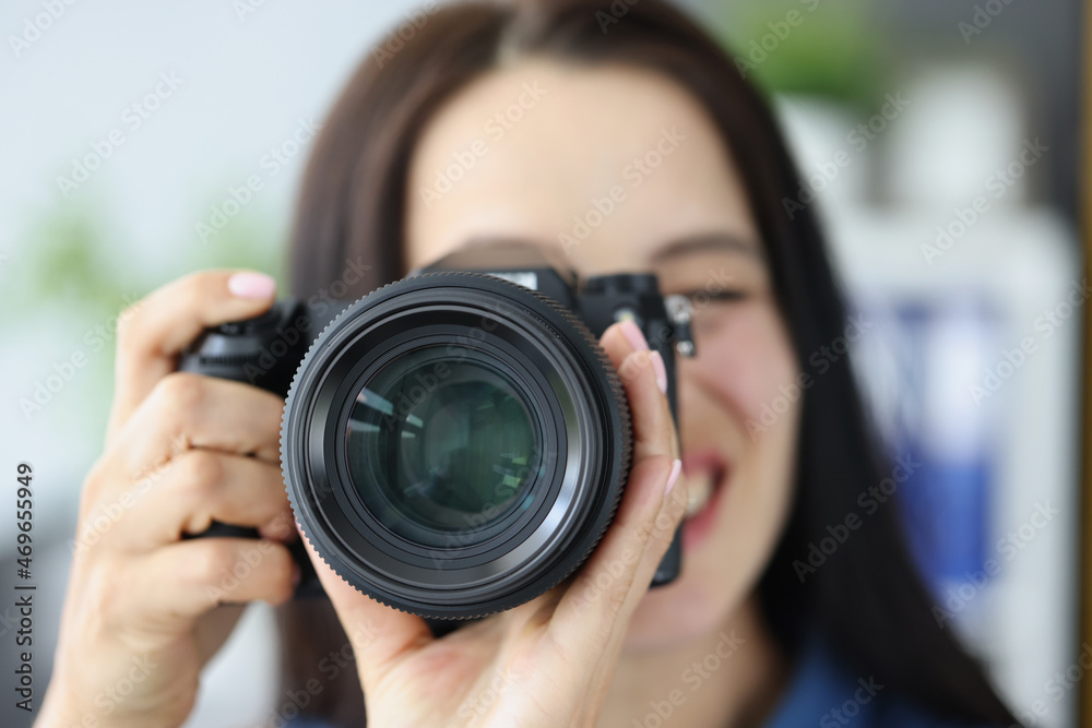 Smiling brunette female photographer pointing super wide lens at you Smiling brunette female photographer pointing super wide lens at you