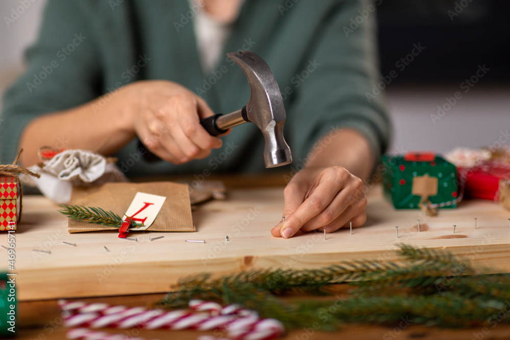 Obraz premium winter holidays and hobby concept - close up of woman with hammer hammering nails in wooden board and making advent calendar at home
