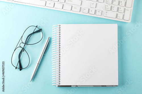 Keyboard, notebook,pen and glasses on the blue background